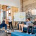 three men sitting while using laptops and watching man beside whiteboard